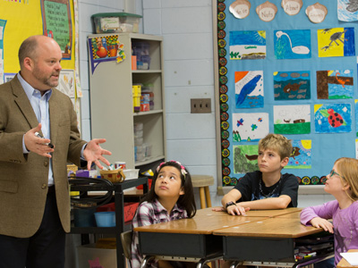An engaging teacher speaks to children in a colorful elementary classroom.