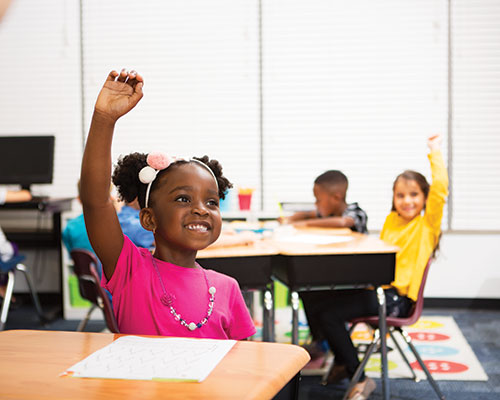 Students raising their hands in a classroom.